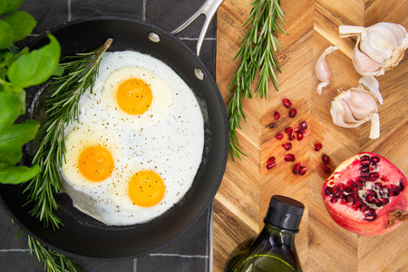 breakfast or brunch, fried eggs in black pans and red pomegranate with garlic and basil. view from the top.の写真素材