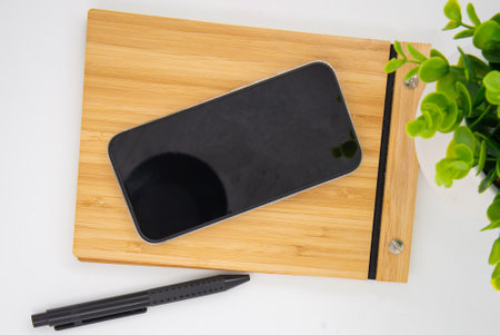 Flat lay of mobile smart phone with blank screen of gadget on notebook. Digital cell phone with copy space area on white background with pencil and leafの写真素材