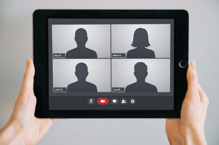 Close-up of hands holding a tablet displaying a video conference interface with silhouette avatars...