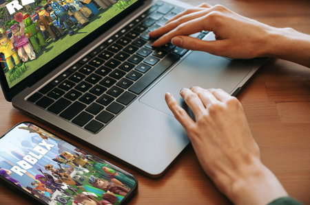 Riga, Latvia - February 2, 2026: Close-up of hands using a laptop while Roblox is displayed on...