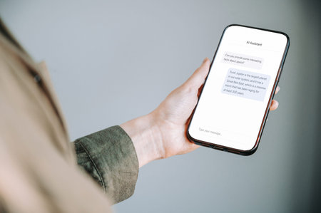 Close-up of a woman holding a smartphone displaying an AI assistant chat conversation. Modern...