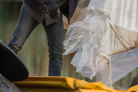 Close-up of an industrial worker pouring plastic granules from a bulk bag into a container at a...