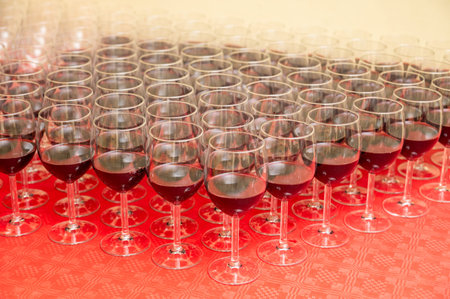 Multiple red wine glasses arranged in neat rows on a red tablecloth, ready for a reception or...