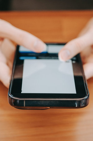 Close-up of hands using a smartphone and credit card on a wooden table, illustrating online payment,...