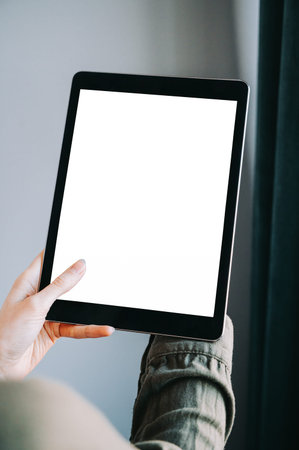 Close-up of a person holding a tablet with blank white screen indoors. Minimal, modern composition...