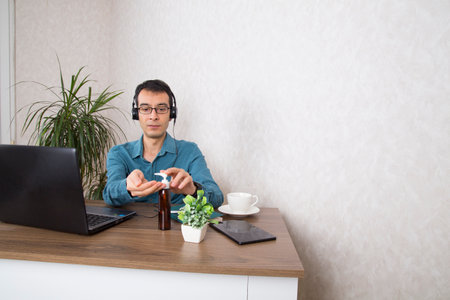 male working from home spraying antiseptic on hands to protect against corononavirus