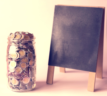 glass jar with a lot of mexican pesos coins and blackboard with vintage color tone processの写真素材