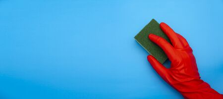 concept image of hand in red rubber protecting glove holding sponge with green fiber isolated on classic blue backgroundの写真素材