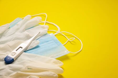 medical latex gloves, protective masks and digital thermometer for protection on yellow background. Useful for pandemic prevention conceptの写真素材