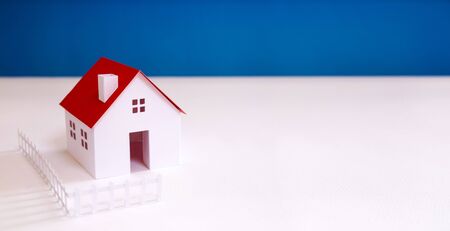 white paper miniature house with red roof on blue color backgroundの写真素材