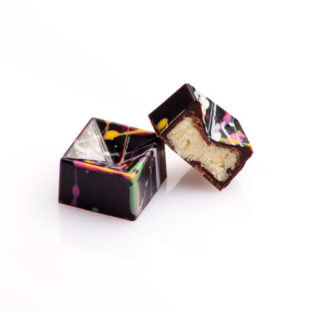 geometric shaped luxury chocolate handmade candy bonbons stuffed with coconut ganache decorated with colorful abstract art on white backgroundの写真素材