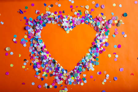 love concept image of heart shape frame made of colorful confetti on orange paper texture backgroundの写真素材