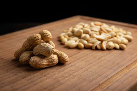 peeled and unpeeled peanuts seeds and on bamboo cutting table with black background. (arachis hypogaea) Edible seeds. Healthy snack nutrition conceptの写真素材