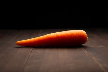 image of a carrot close up on rustic wooden surface and black backgroundの写真素材