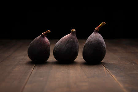 image of three common figs fruits close up on rustic wooden surface and black background