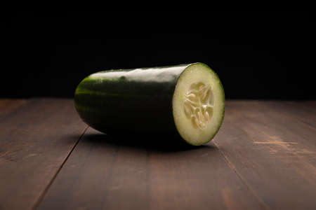 still life image of half cucumber close up on rustic wooden surface and black backgroundの写真素材