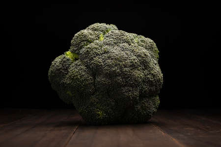 still life image of raw broccoli head crown close up on rustic wooden surface and black backgroundの写真素材