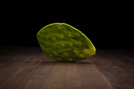 still life image of one organic nopal pad from Mexico. Raw and clean no spikes ready to cook. Close up on rustic wooden surface and black backgroundの写真素材
