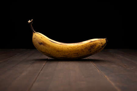 image of ripe yellow banana close up on rustic wooden surface and black backgroundの写真素材