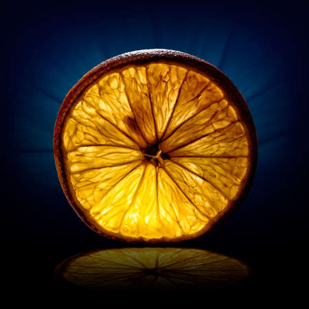 creative image of a slice of orange view on backlight on dark blue backgroundの写真素材