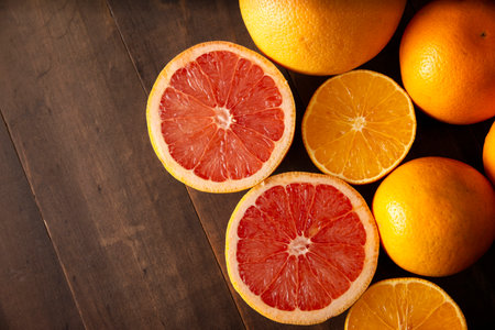 flat lay image of ripe orange and grapefruit slices and several whole oranges on brown rustic wooden table with copy spaceの写真素材