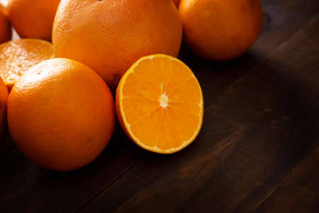 close up of a ripe orange cut in half and several whole oranges on brown rustic wooden table with copy spaceの写真素材