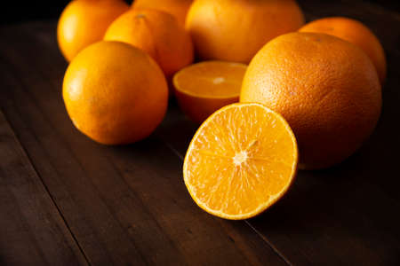 close up of a ripe orange cut in half and several whole oranges on brown rustic wooden table with copy spaceの写真素材
