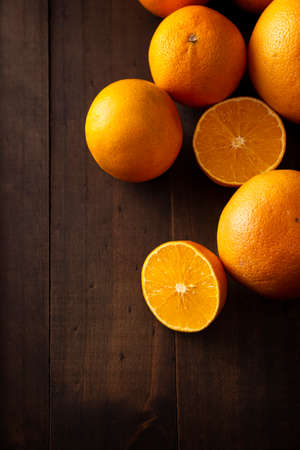 a ripe orange cut in half and several whole oranges on brown rustic wooden table with copy spaceの写真素材