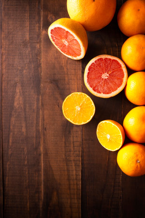 flat lay image of ripe orange and grapefruit slices and several whole oranges on brown rustic wooden table with copy spaceの写真素材