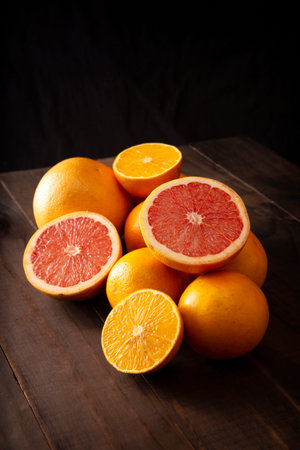 ripe orange and grapefruit slices and several whole oranges on brown rustic wooden table and black backgroundの写真素材