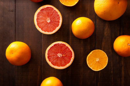 top view image of ripe orange and grapefruit slices and several whole oranges on brown rustic wooden tableの写真素材
