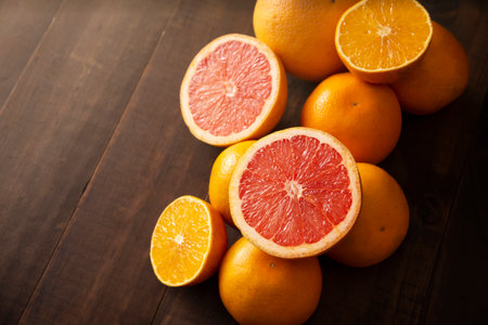 half cut ripe orange and grapefruit and several whole oranges on brown rustic wooden table with copy spaceの写真素材