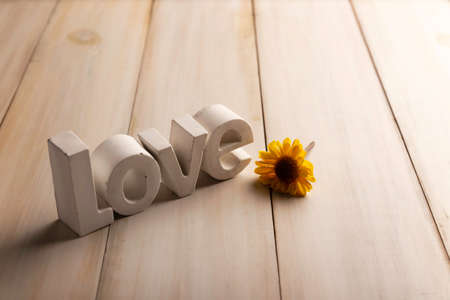 Concrete letters saying Love with a yellow flower on white washed wooden boardの写真素材