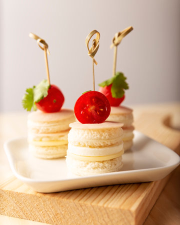 Delicious Party Snacks. Round mini sandwiches with ham and cheese decorated with cherry tomato on a bamboo stickの写真素材