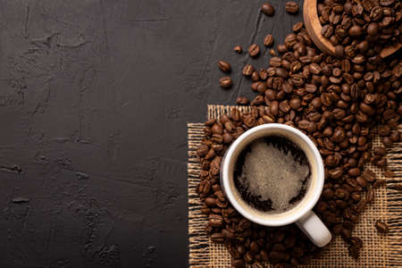 White lungo cup with hot coffee drink and toasted coffee beans scattered on a rustic black table. Top view with Copy space for your textの写真素材