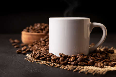 White lungo cup with hot coffee drink and toasted coffee beans scattered on a rustic black table. Close up image. Blank cup for copy spaceの写真素材