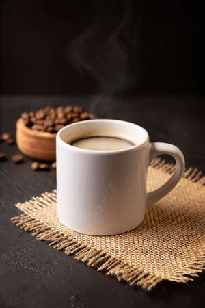 White lungo cup with hot coffee drink and toasted coffee beans scattered on a rustic black table. Close up image. Blank cup for copy spaceの写真素材