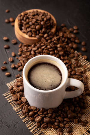 Coffee beans scattered on a rustic black table and white lungo cup with hot coffee drink. Close up imageの写真素材