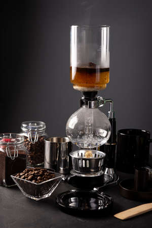 Vacuum coffee maker also known as vac pot, siphon or syphon coffee maker and toasted coffee beans on rustic black stone table.の写真素材