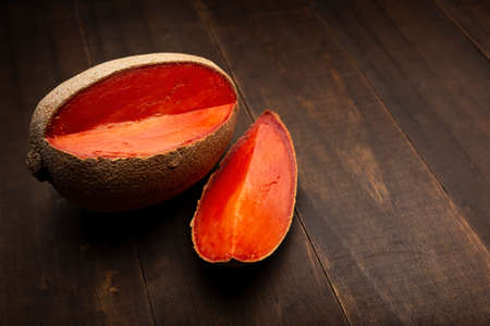 still life image of one mexican red mamey close up on rustic wooden surface and black backgroundの写真素材