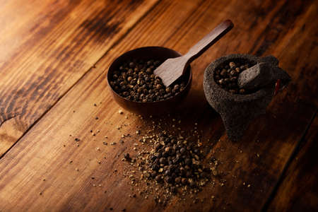 Black pepper grains in a small Molcajete (traditional Mexican version of the mortar and pestle) and small bowl on rustic wooden background.の写真素材