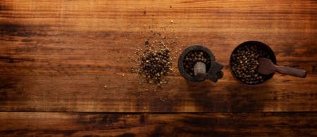 Black pepper grains in a small Molcajete (traditional Mexican version of the mortar and pestle) and small bowl on rustic wooden background.の写真素材