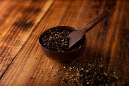 Black pepper seeds in a small wooden bowl on a rustic wooden table. close-upの写真素材