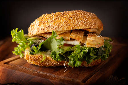 Healthy homemade sandwich with grilled chicken breast, lettuce, avocado, alfalfa germ and various other vegetables on rustic wooden boardの写真素材