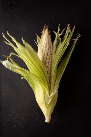 Top View Image of raw white corn on the cob on black rustic surface. copyspace. close up. Flat lay.の写真素材