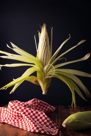 creative image of raw white corn on the cob levitating on wooden rustic table.の写真素材