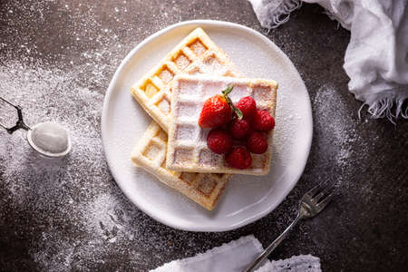 Top View of Homemade waffles with strawberries, raspberries and powdered sugar on white dish. Flat lay.の写真素材