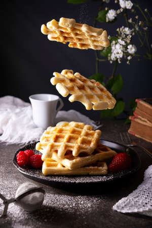 Homemade waffles floating with icing sugar and fruits.の写真素材