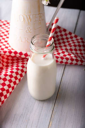 Fresh milk in little glass bottle with red and white biodegradable stripped paper straw on wooden rustic white surfaceの写真素材
