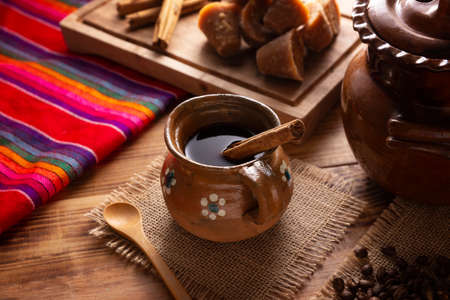 Coffee pot. Traditional Mexican coffee and basic ingredients for its preparation, coffee, cinnamon and piloncillo, served in a clay cup called "jarrito" on a rustic wooden surface.の写真素材